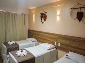 Habitación de hotel con dos camas, cada una con cubrecama y almohadas blancas, y cabeceros de madera. Hay luces fijadas a la pared y un adorno en forma de corazón en la pared.