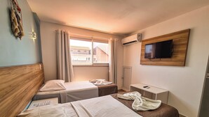 A hotel room with two beds, a TV mounted on the wall, a window with curtains, and an air conditioning unit. - Pousada Jardins Tropical (Ipojuca)