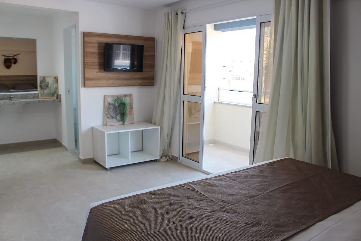 A bedroom with a bed, a TV mounted on the wall, a small white console table, and a sliding glass door to a balcony.