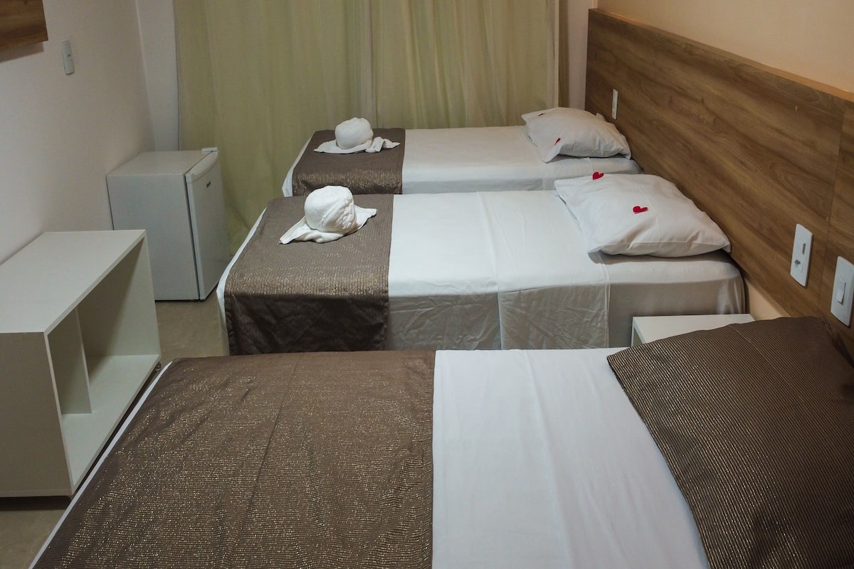 A hotel room with two beds, each with a brown headboard and white bedding. There are two bedside tables and a small bedside lamp.
