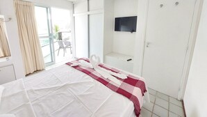 A hotel room with a bed, a TV, a balcony with chairs, and a door. - Ancorar Flat Resort (Ipojuca)