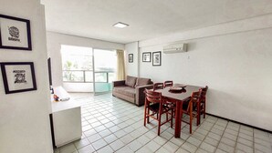A dining area with a table and chairs, a sofa, and a window with a view. - Ancorar Flat Resort (Ipojuca)