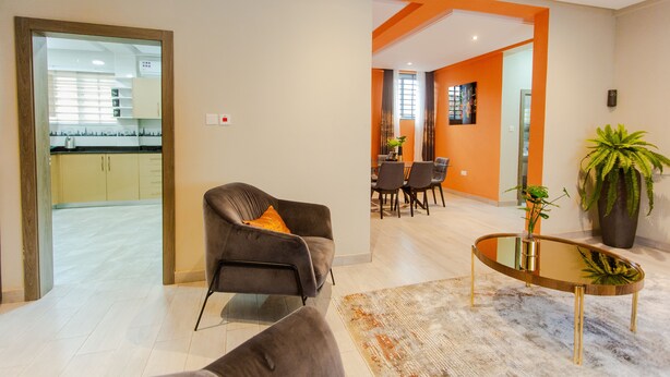 Una sala de estar moderna con un sofá, una mesa de centro de vidrio y un área de comedor al fondo.