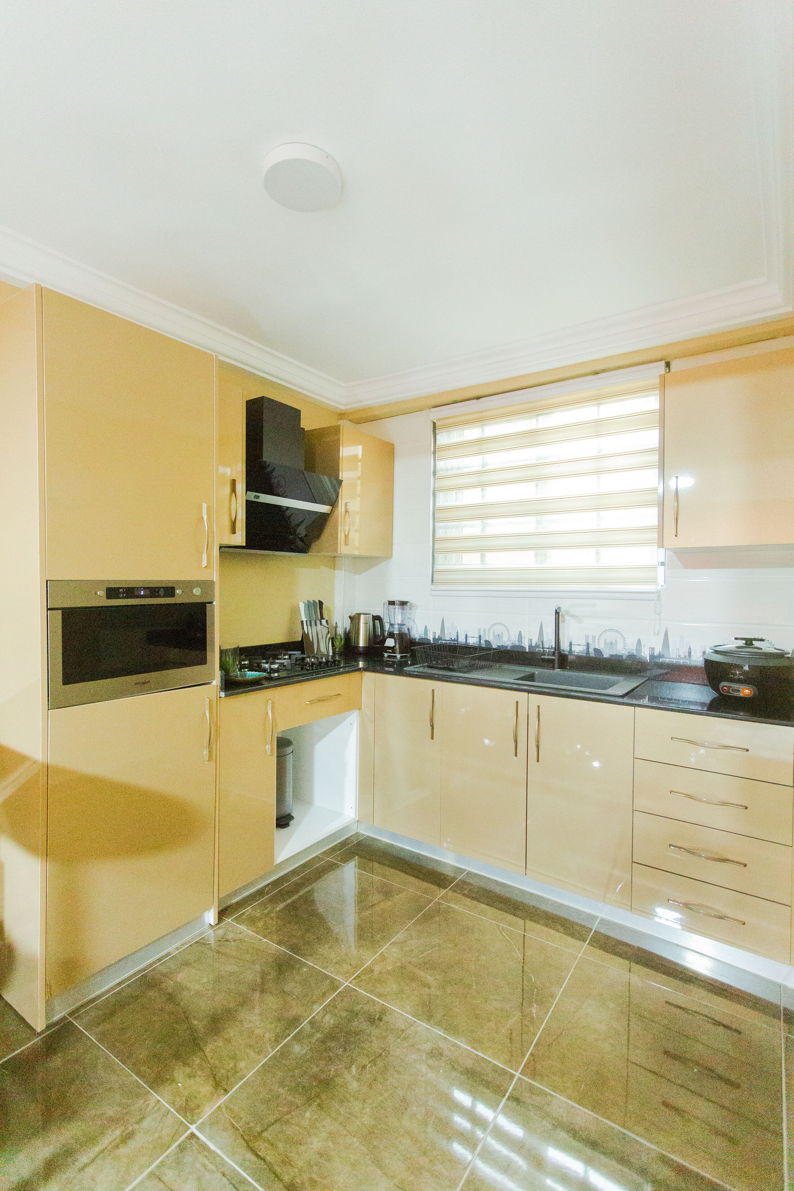A kitchen with beige cabinets, a stove, and a window with blinds.