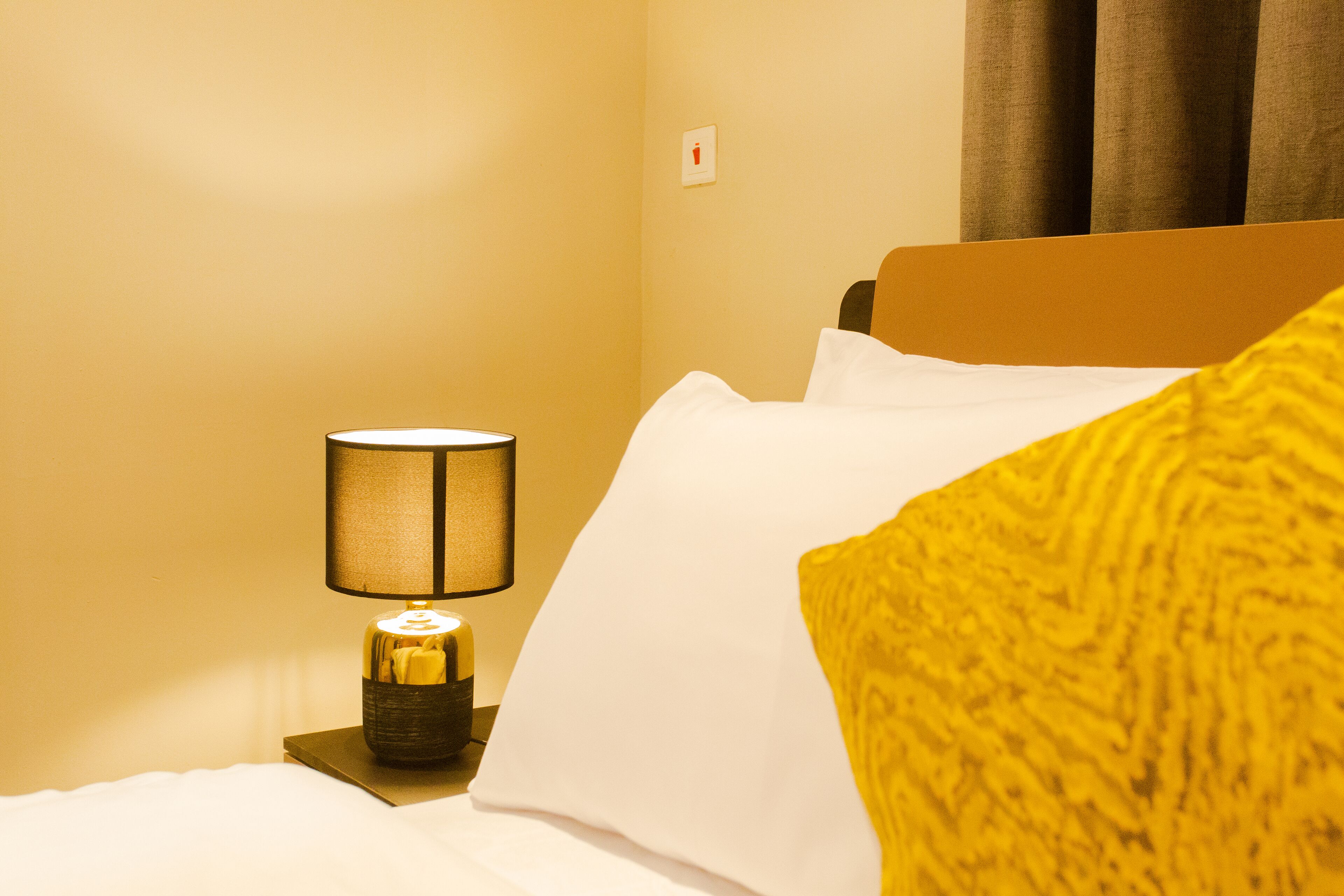 A hotel room with a bed, a nightstand with a lamp, and a window with curtains.