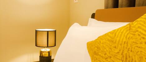 A hotel room with a bed, a nightstand with a lamp, and a window with curtains.
