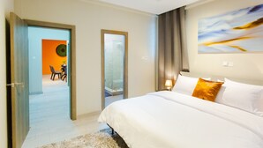 Una habitación de hotel con una cama, un cuadro en la pared y vistas al comedor a través de una puerta abierta.