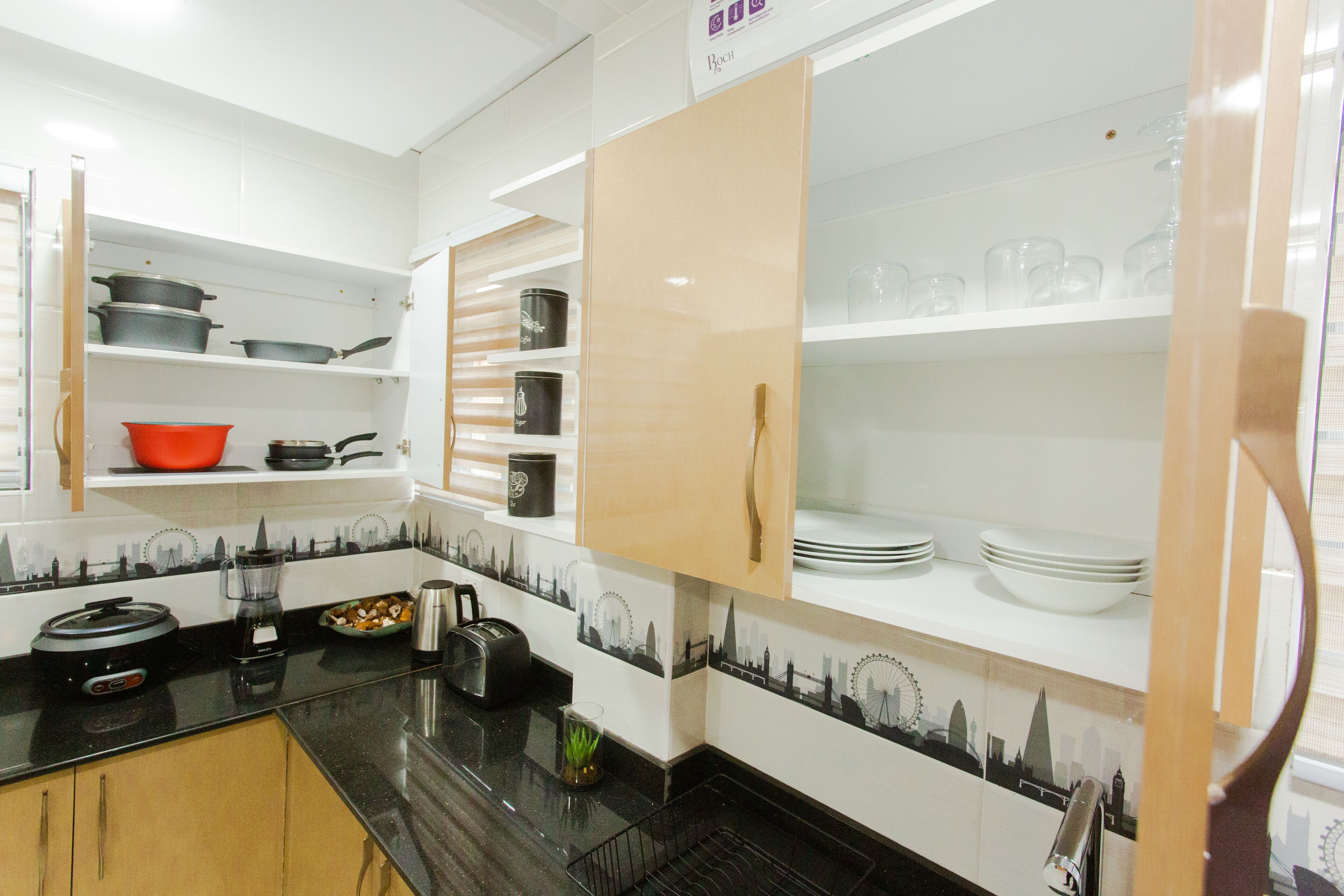 A kitchen with white cabinets, black countertops, and a cityscape backsplash.