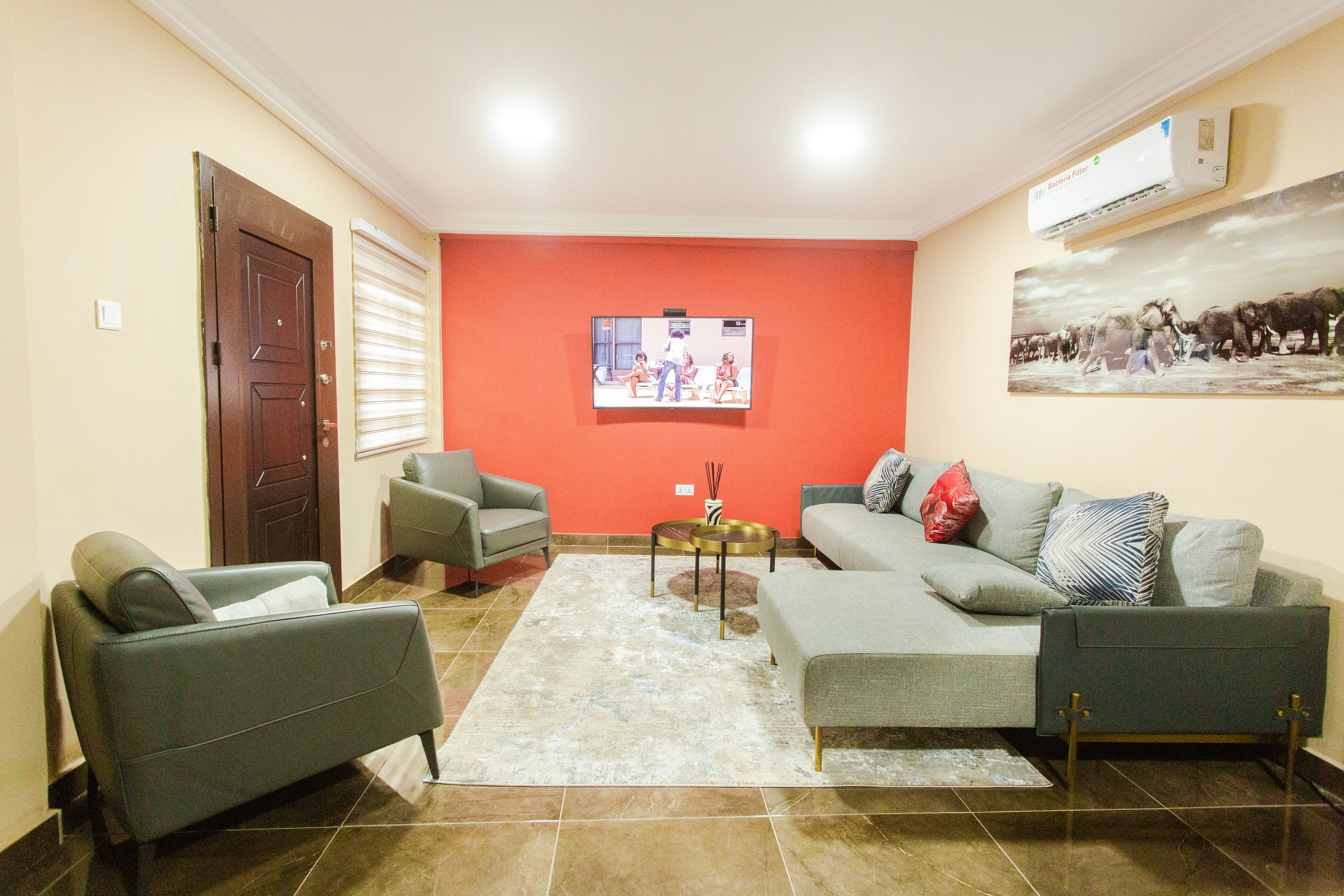 A living room with a sofa, two armchairs, a coffee table, and a TV mounted on the wall.