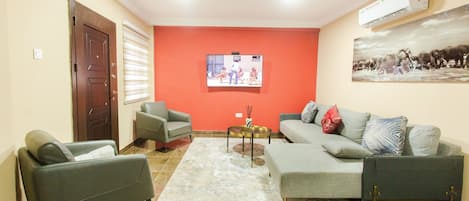 A living room with a sofa, two armchairs, a coffee table, and a TV mounted on the wall.