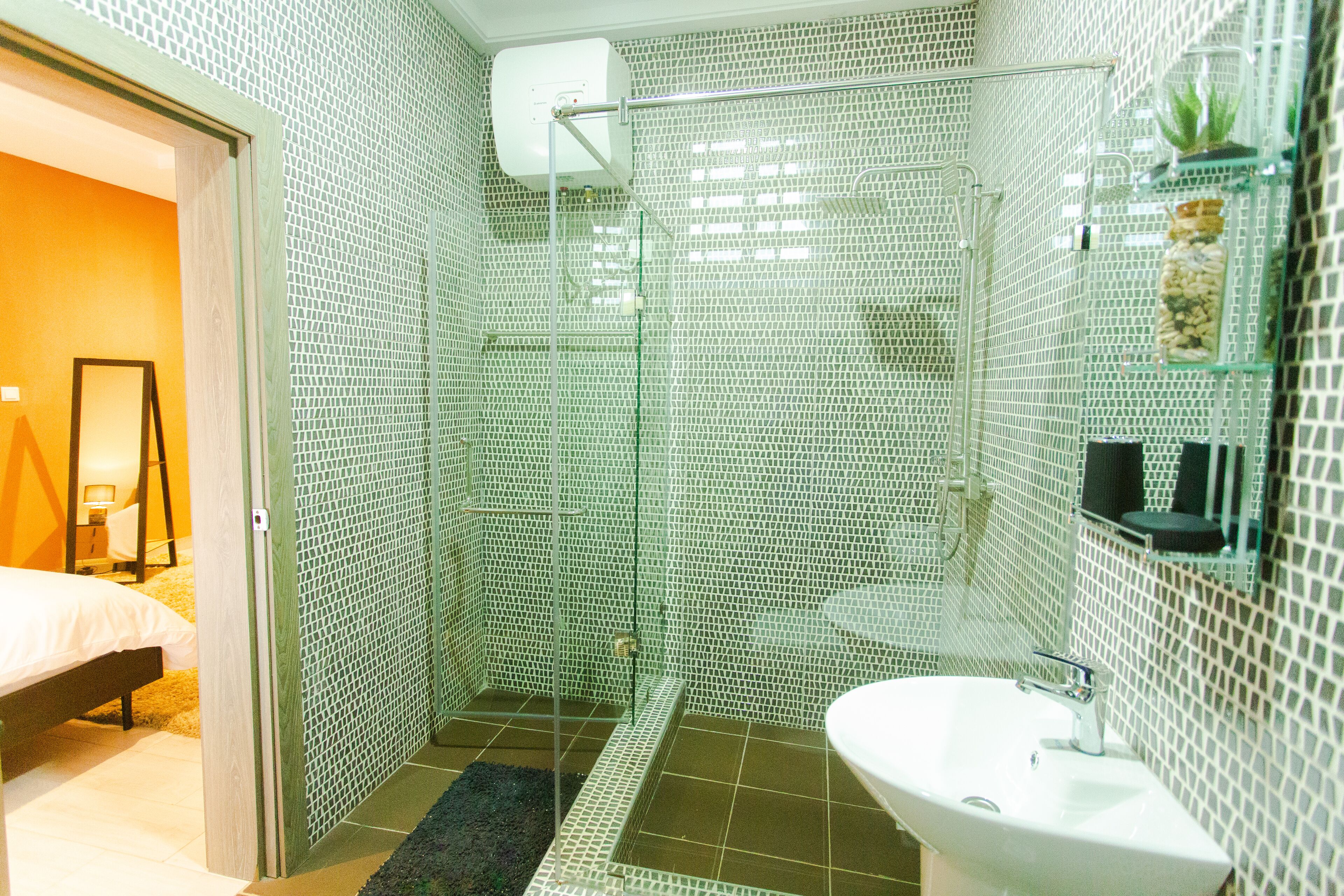 Un baño moderno con cabina de ducha de vidrio, un lavabo blanco y un pequeño estante con artículos de aseo.