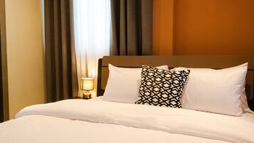 A neatly made bed with white linens and two patterned pillows, a bedside lamp, and a window with curtains.