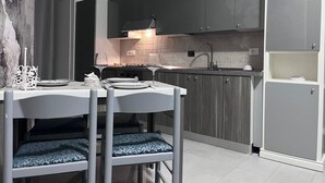 A modern kitchen with grey cabinets, a white dining table with blue cushioned chairs, and a sign above the cabinets reading "Nina's House". - Nina's house 3 300 meters from the sea (Santa Caterina Dello Ionio Marina)