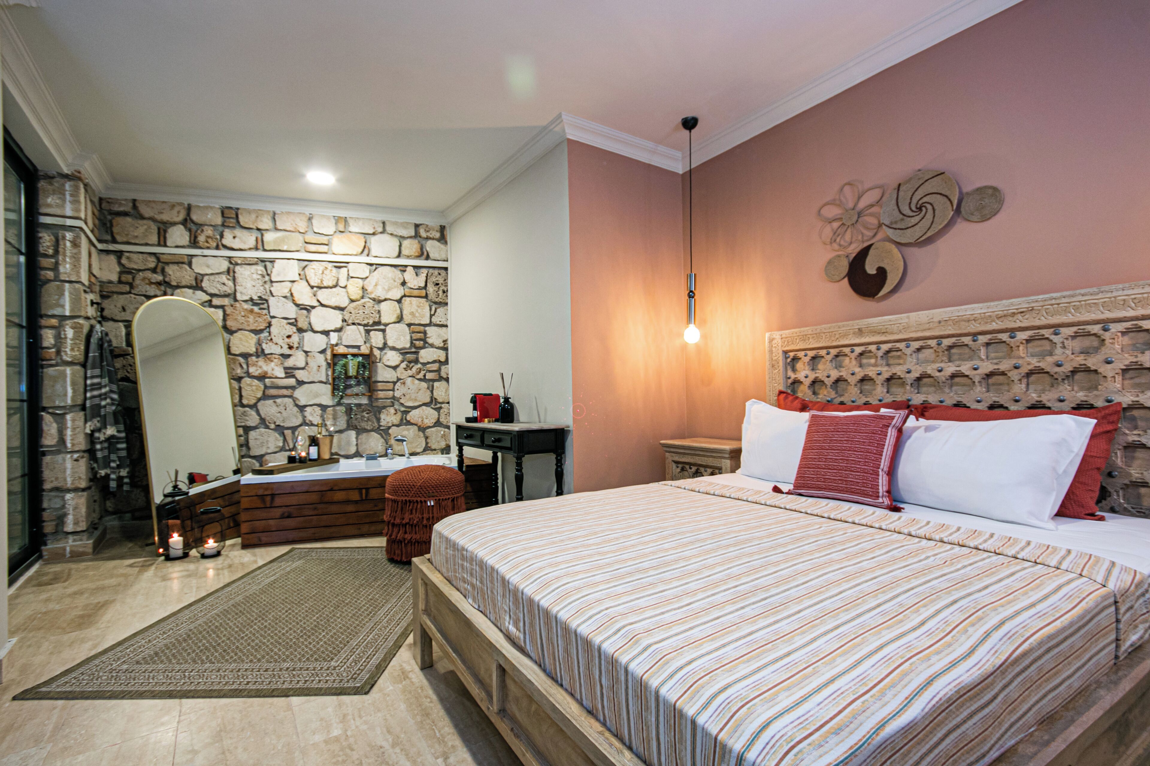 A bedroom with a stone wall, a wooden bed, a stone fireplace, and a mirror.