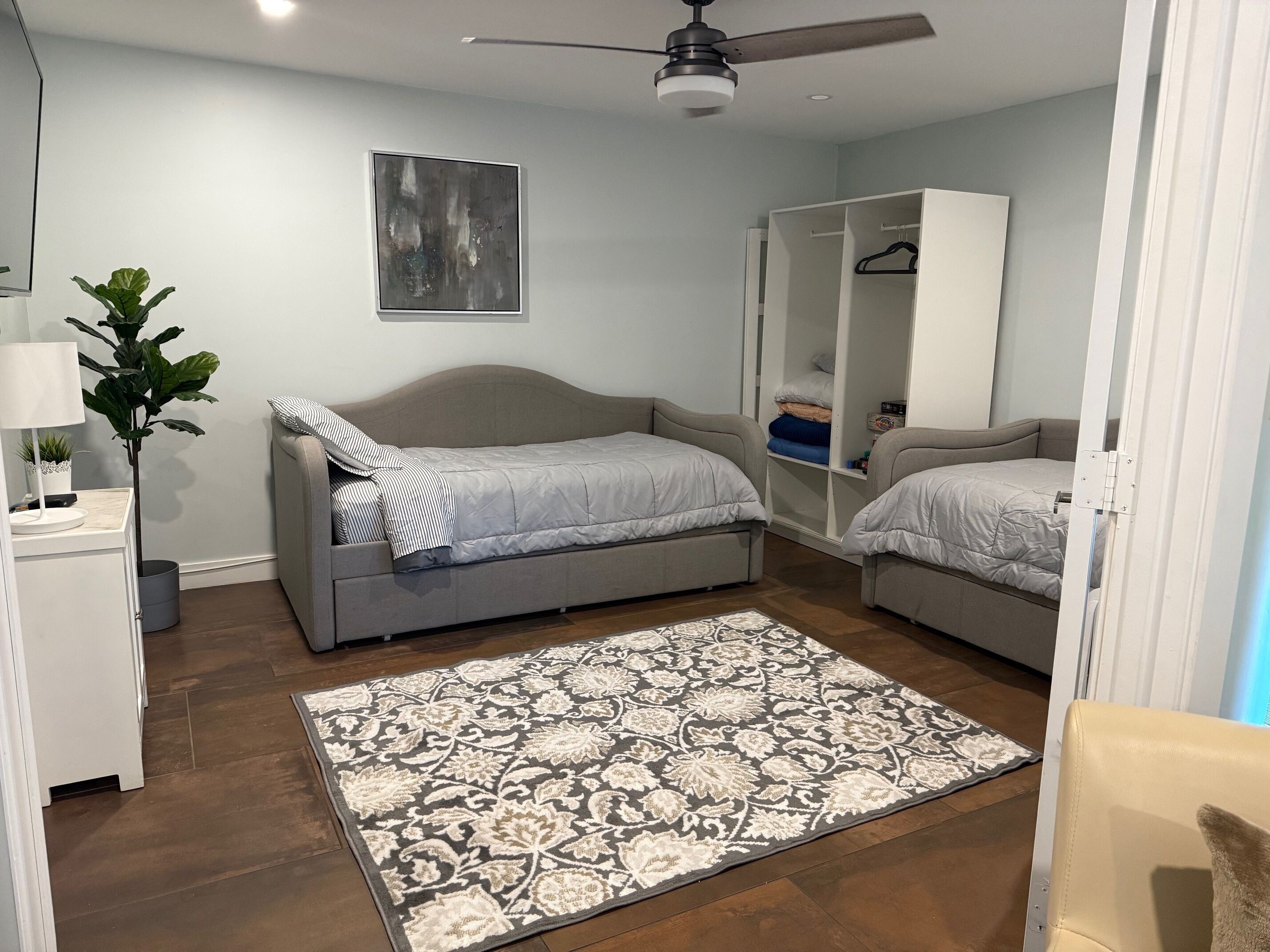 A bedroom with two beds, a wardrobe, a ceiling fan, a floor lamp, and a large patterned rug.