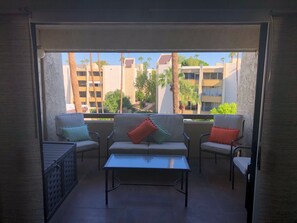 An outdoor balcony with a sofa set, a table, and a view of buildings and palm trees. - Gorgeous Condo by Fashion Square/Old Town w/pool (Scottsdale)