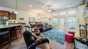 A spacious living area with a large leather sofa, a kitchen with wooden cabinets, and a dining area with a bar. - Quiet, Beautiful Home Nestled in the woods (Hot Springs Village)