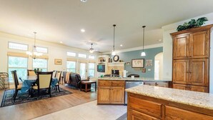 A spacious kitchen with wooden cabinets, a granite countertop, and a dining area with a table and chairs. - Quiet, Beautiful Home Nestled in the woods (Hot Springs Village)