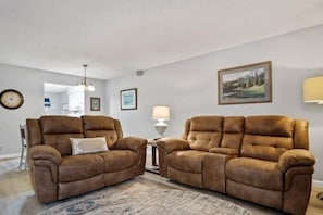 A living room with two brown sofas, a patterned rug, a lamp, and a clock on the wall.