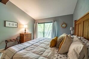 Een slaapkamer met een bed, een kaptafel, een lamp, een raam met gordijnen en een spiegel aan de muur.