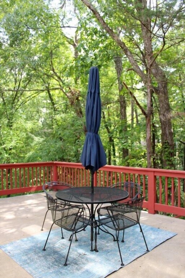 An outdoor patio with a round metal table and chairs, a blue umbrella, and a red railing.
