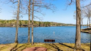Un área de picnic junto al lago con una mesa y banco de madera, rodeada de árboles y con vistas a un lago tranquilo.