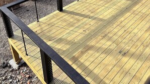 En træterrasse med gelænder i metal, med udsigt over vand, og et overdækket fortøjningsområde i baggrunden.