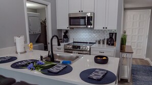 Une cuisine moderne avec des meubles blancs, un four à micro-ondes en acier inoxydable et une cuisinière à gaz.