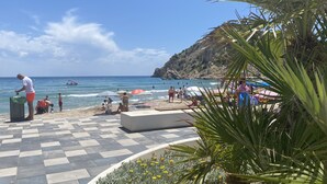 Una playa con un paseo adoquinado, sombrillas y gente disfrutando del mar.