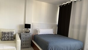 A bedroom with a bed, a nightstand, a lamp, a bedside table, and a chair.