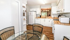 Une cuisine moderne avec des meubles blancs, un plan de travail en bois et une table à manger en verre, accompagnée de chaises en osier.