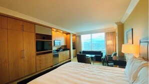 Habitación de hotel con una cama grande, kitchenette, zona de estar con vistas y un ventanal amplio.