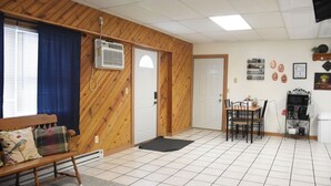 A room with a wooden wall, a dining table with chairs, a bench, a microwave, and a coffee machine.