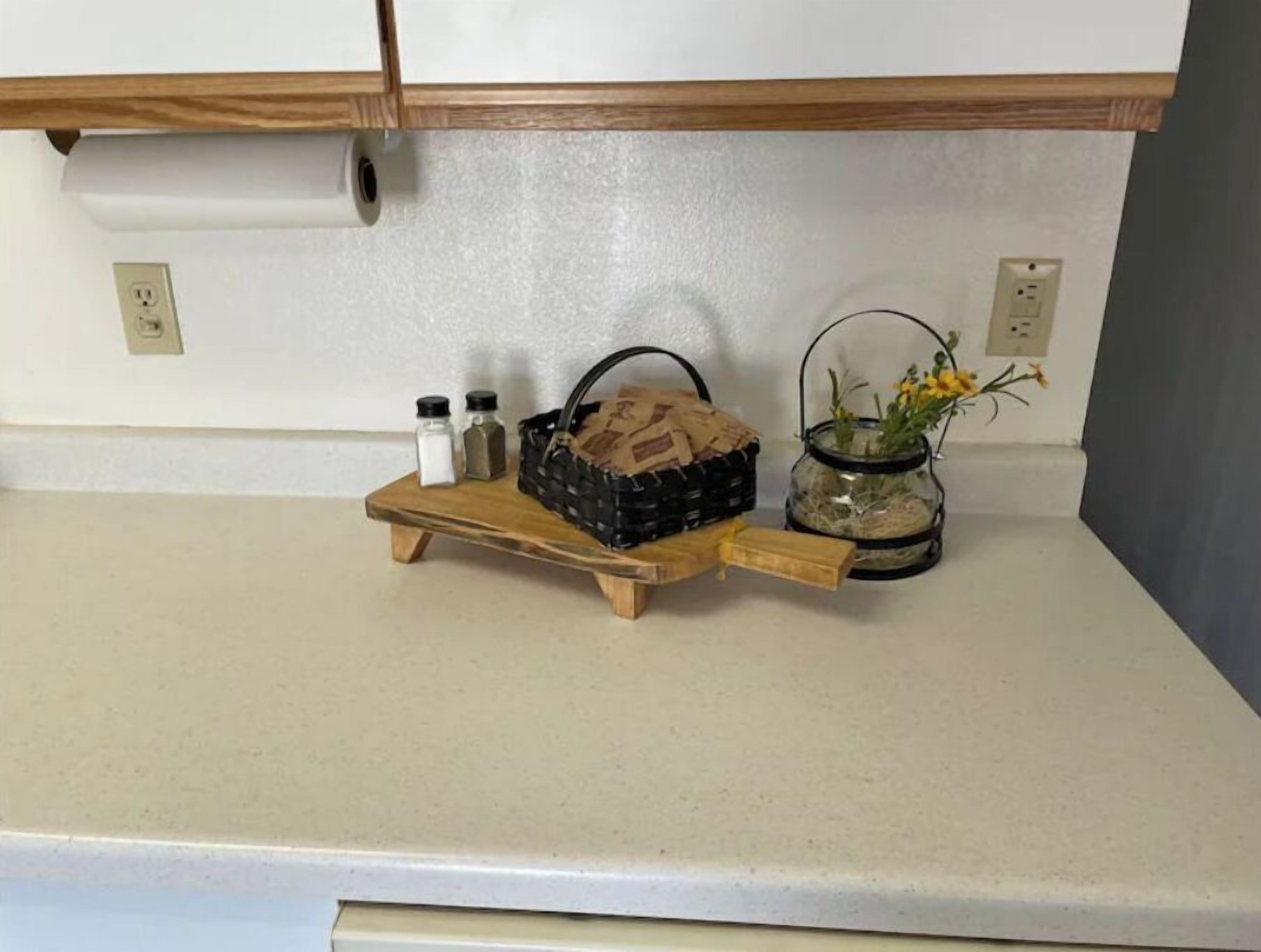 Eine Küchenarbeitsplatte mit einem Holztablett, das einen Korb, Salzstreuer und ein Glas mit Blumen enthält.