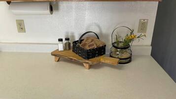 Eine Küchenarbeitsplatte mit einem Holztablett, das einen Korb, Salzstreuer und ein Glas mit Blumen enthält.