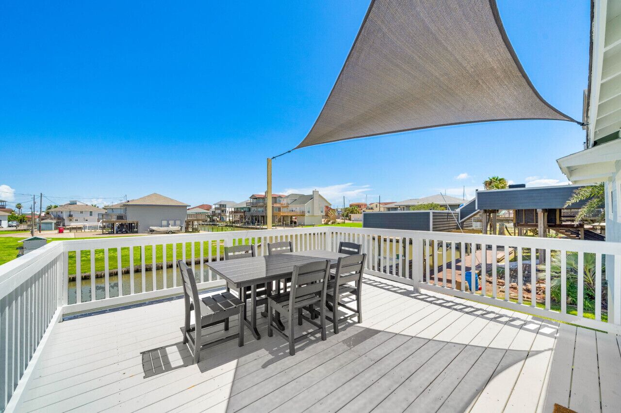 Una terraza con una mesa y sillas, rodeada por una barandilla blanca, con vistas a una zona residencial.