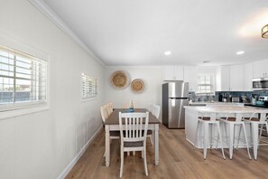 Una cocina moderna con muebles blancos, una isla central con taburetes de bar y un refrigerador de acero inoxidable.