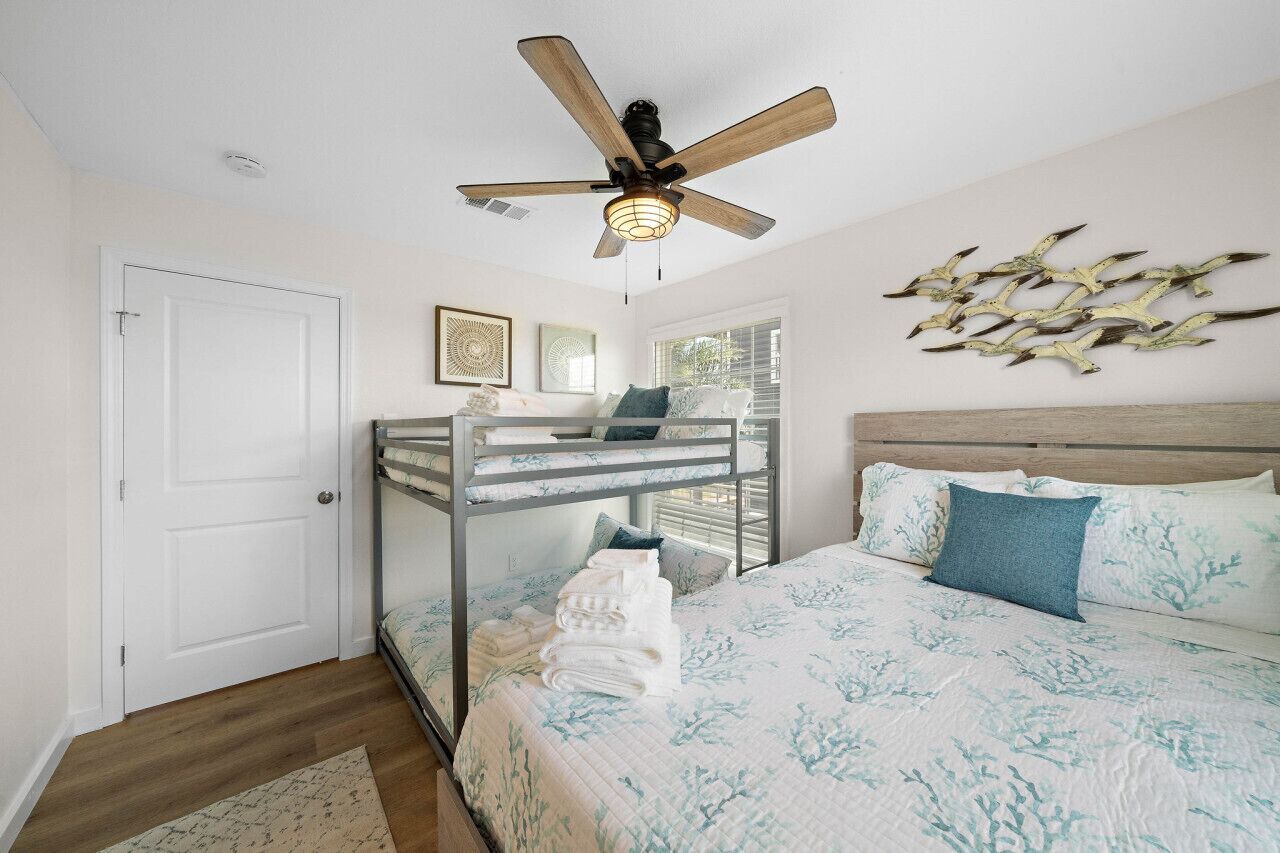 Un dormitorio con una cama litera, un ventilador de techo, una cama con colcha estampada y decoración en las paredes.