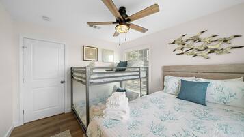 Un dormitorio con una cama litera, un ventilador de techo, una cama con colcha estampada y decoración en las paredes.
