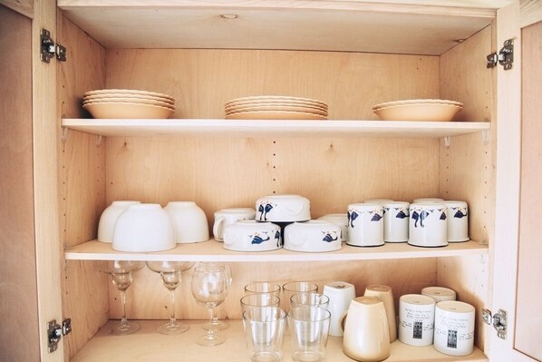 Un mueble de madera con estantes que contienen cuencos, platos, vasos y velas.