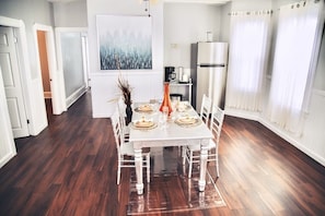 Un comedor con una mesa blanca dispuesta para cuatro personas, rodeada de sillas blancas. Un cuadro grande cuelga de la pared sobre la mesa.