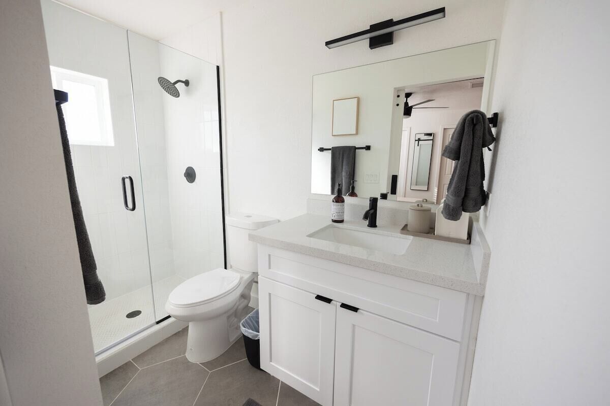 Une salle de bain moderne avec une douche à parois de verre, des toilettes blanches et un meuble-lavabo avec un miroir.