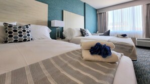 Habitación de hotel con dos camas, un escritorio, una lámpara y un amplio ventanal con cortinas.