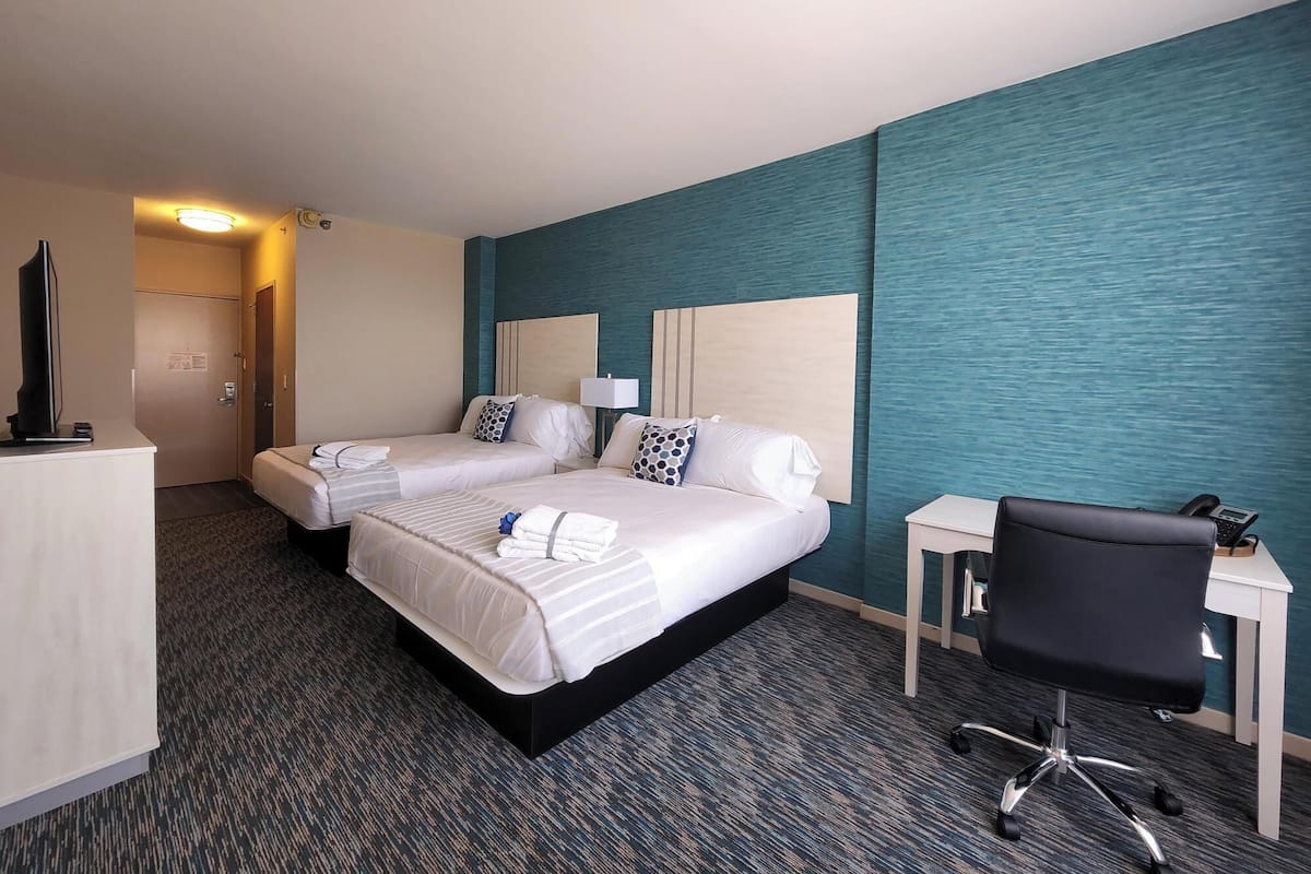 Quarto de hotel com duas camas, uma escrivaninha, uma cadeira e uma televisão.