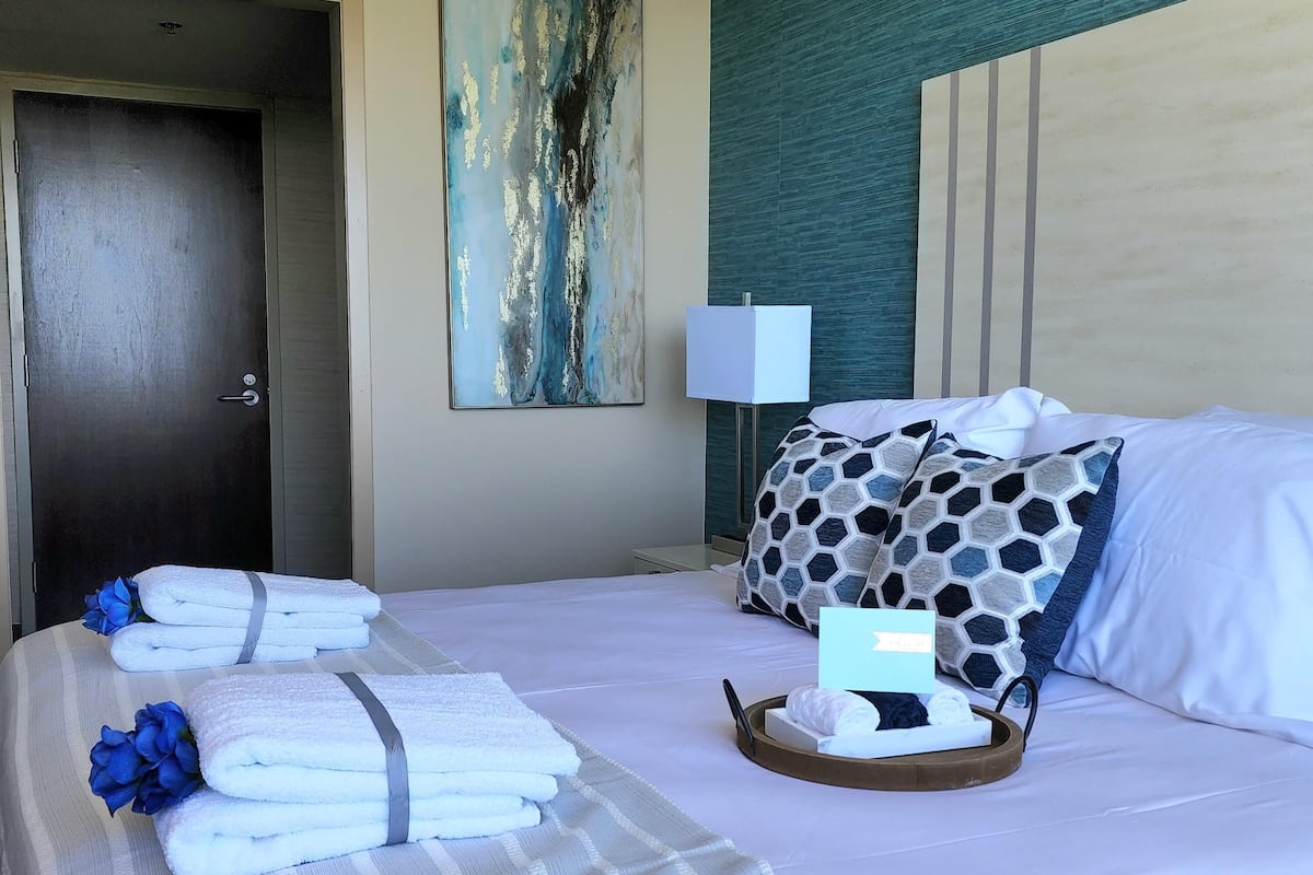 Cama bem arrumada com toalhas e um tabuleiro com artigos de higiene pessoal, uma porta e um quadro na parede.