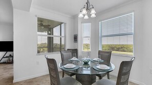 Enjoy meals in this stylish dining area with a round table for four, surrounded by comfortable chairs and large windows offering a view of lush greenery.