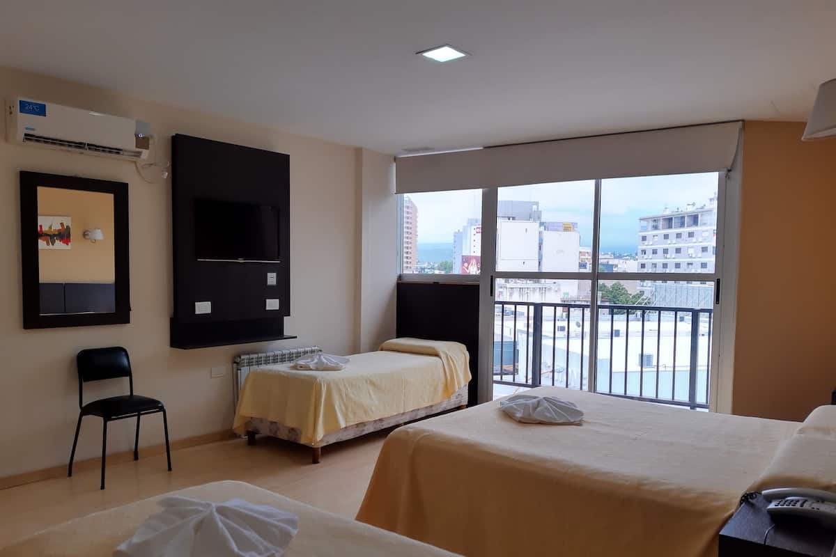 Une chambre d’hôtel avec deux lits, une télévision, une chaise et un balcon donnant sur la ville.