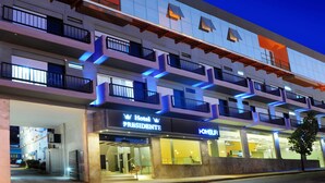 Et hotel med flere etager og balkoner, med et tydeligt skilt 'Hotel Presidente' og et skilt 'OHSUR'.