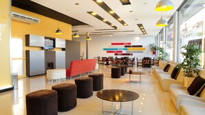 En moderne lobby med en rød sofa, flere siddeområder og et stort vindue med udsigt til gaden.