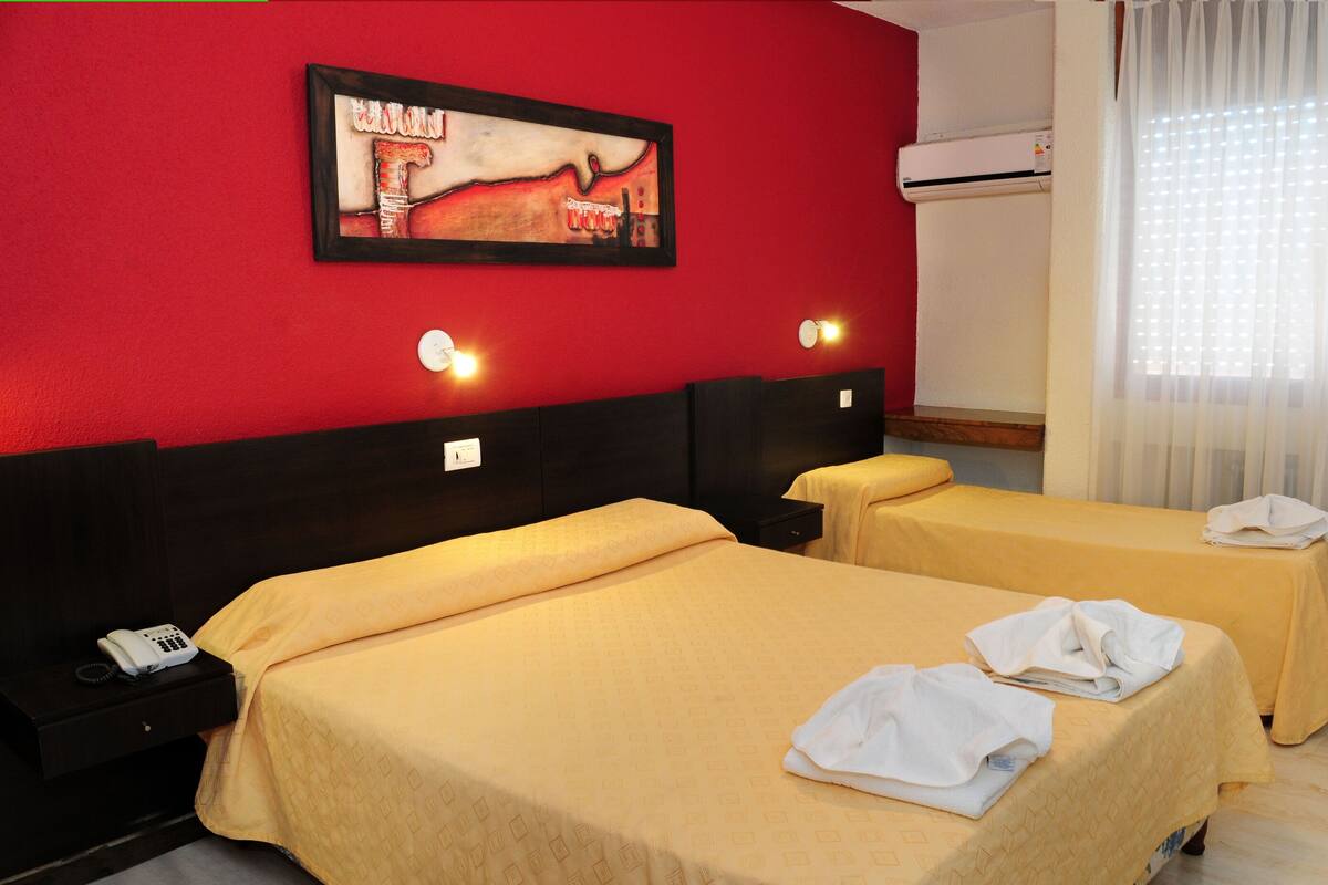 Une chambre d’hôtel avec deux lits, un tableau au mur, une chaise et une fenêtre avec des rideaux.